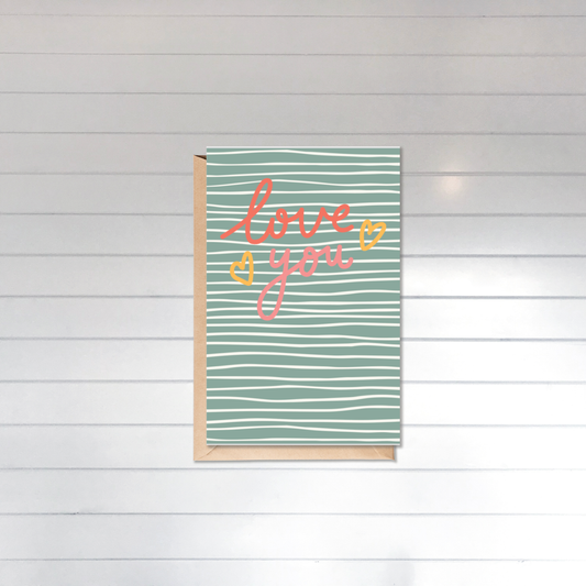 Card with 'love you' text on a striped background against a white wooden panel wall