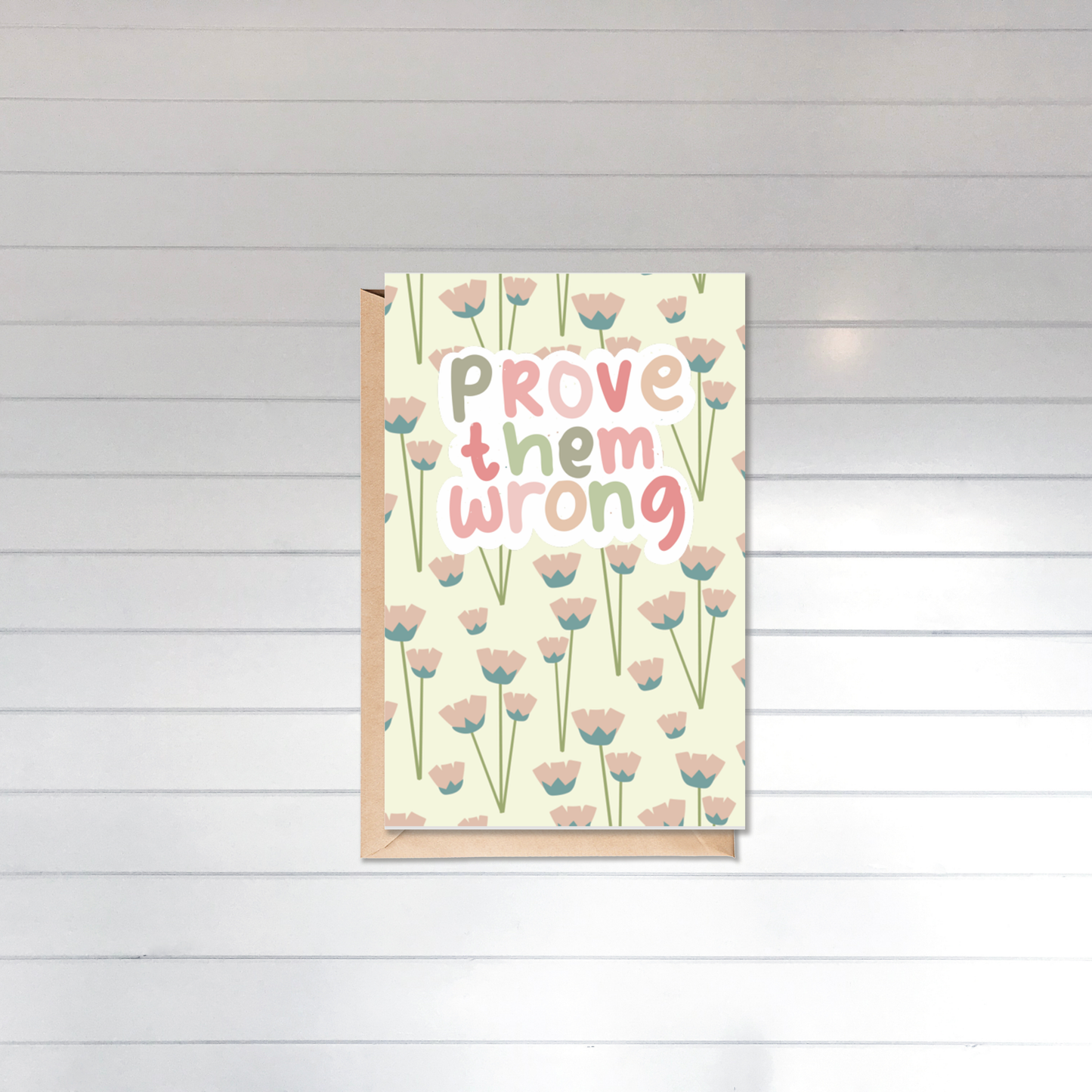 Greeting card with floral design and 'Prove them wrong' text on a wooden surface