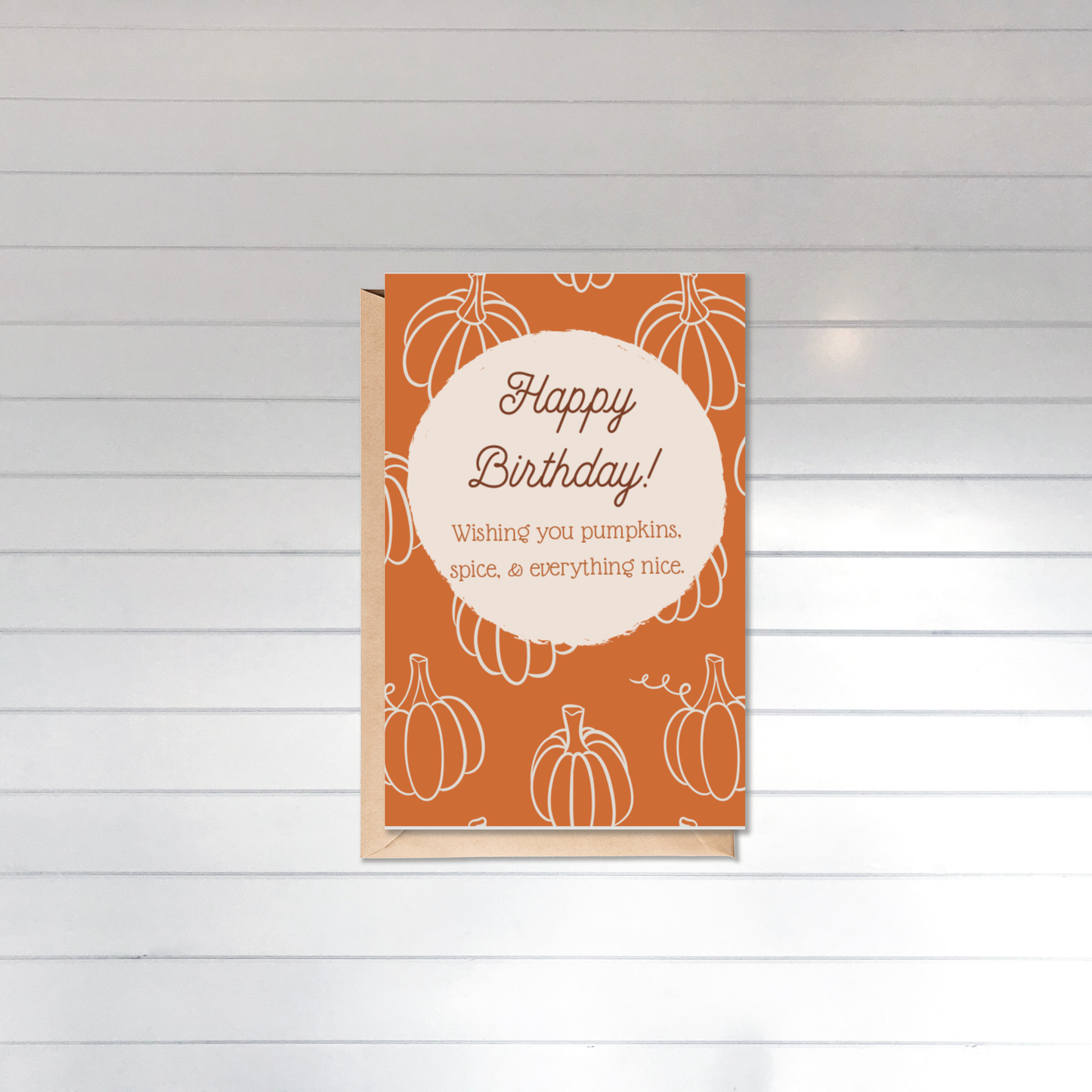 Happy Birthday card with pumpkin design on an orange background, placed on a wooden surface.