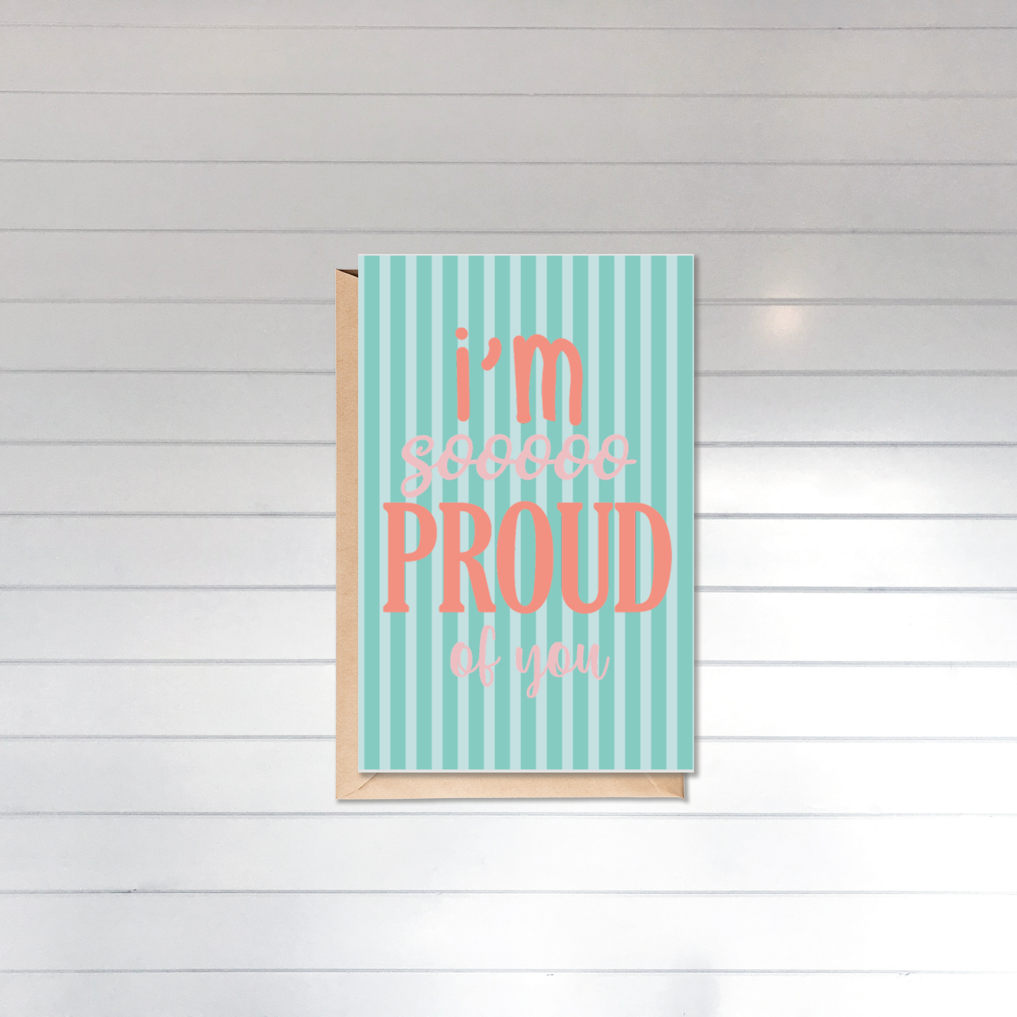 Card with 'I'm so proud of you' text on a striped background against a wooden panel wall.