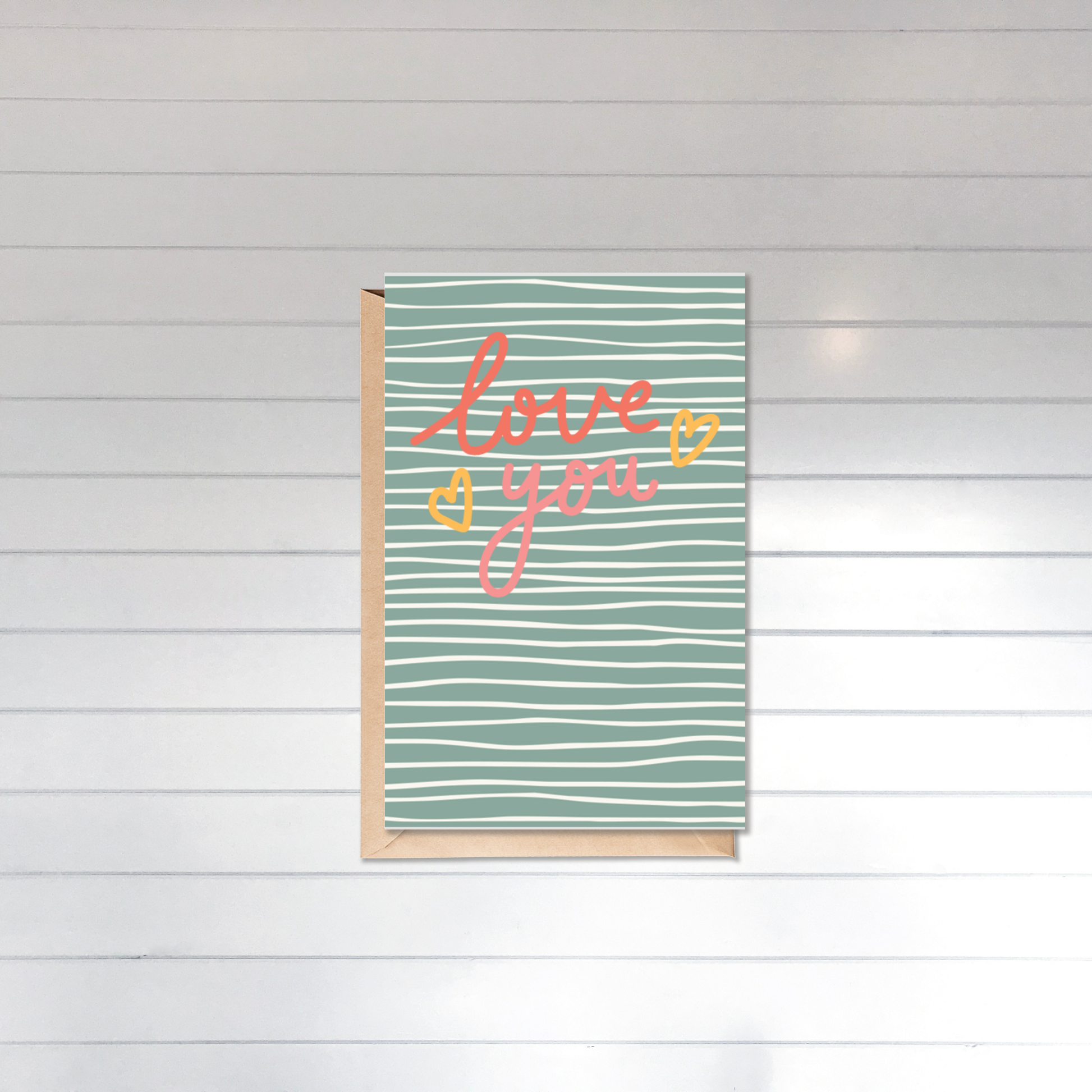Card with 'love you' text on a striped background against a white wooden panel wall